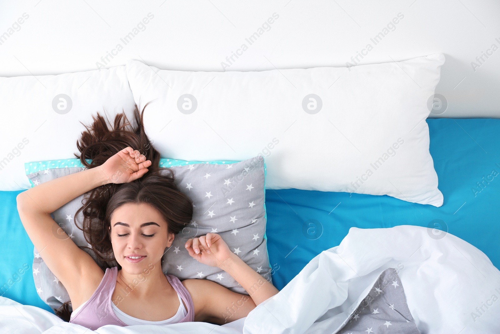 Photo of Young woman sleeping on soft pillow, top view. Bedtime