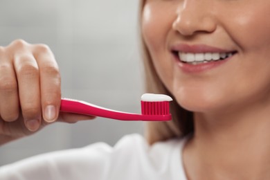 Photo of Woman holding brush with toothpaste in bathroom, closeup