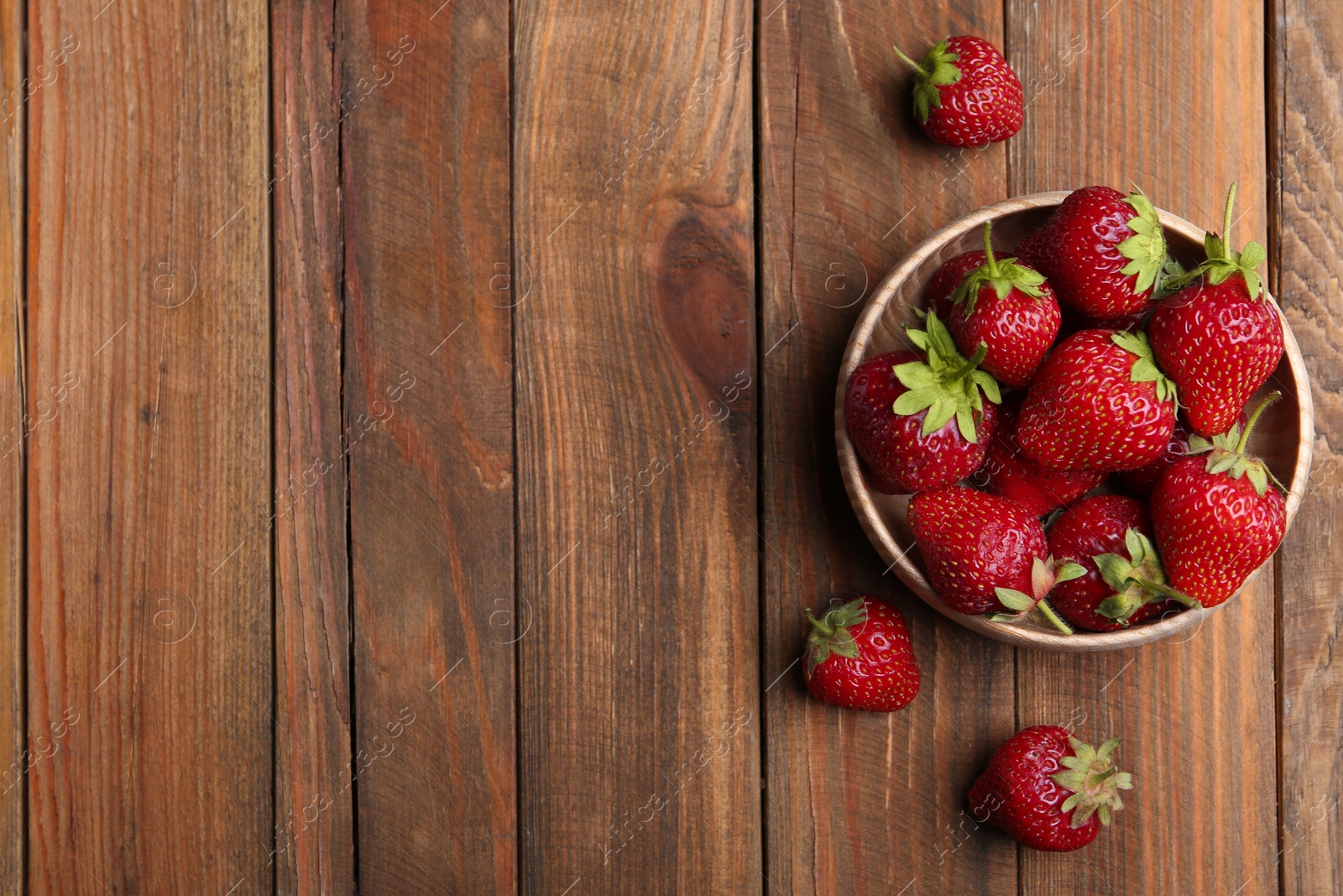 Photo of Delicious ripe strawberries in bowl on wooden table, flat lay. Space for text