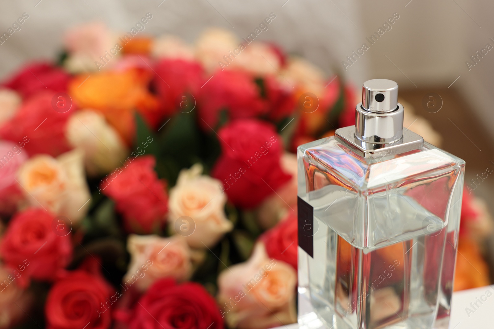 Photo of Bottle of perfume against bouquet of beautiful roses, closeup. Space for text