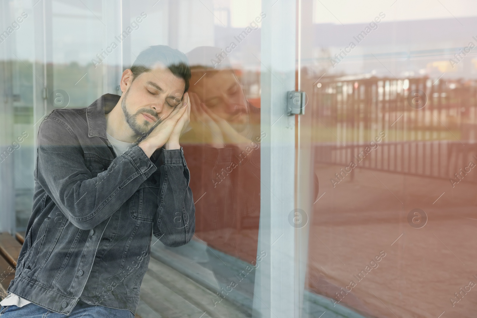 Photo of Tired man sleeping at public transport stop outdoors, view through glass. Space for text