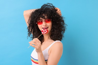 Beautiful woman in sunglasses with lollipop on light blue background