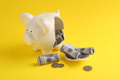 Financial savings. Broken piggy bank, dollar banknotes and coins on yellow background