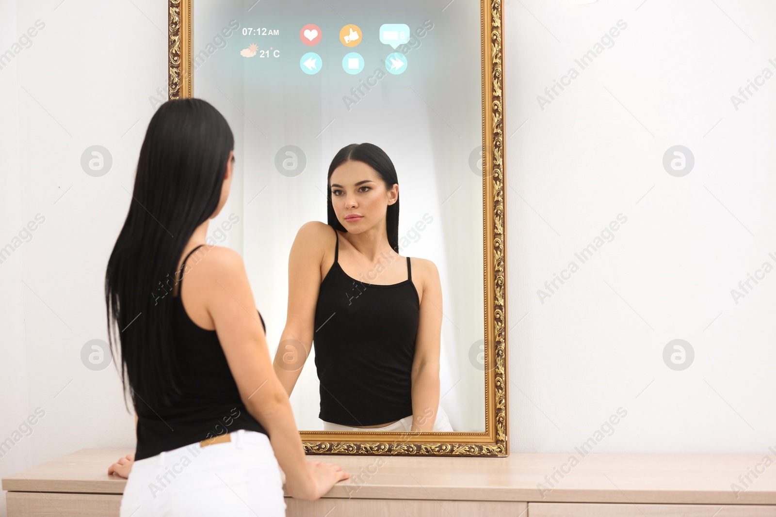 Image of Beautiful young woman looking at herself in smart mirror indoors