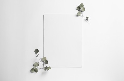 Photo of Empty sheet of paper and decorative eucalyptus leaves on white background, flat lay. Mockup for design
