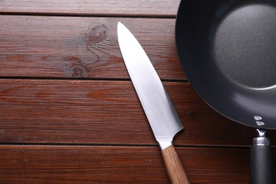 Photo of Empty iron wok and knife on wooden table, flat lay. Space for text