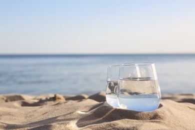 Photo of Sandy beach with glasses of refreshing drink on hot summer day, space for text