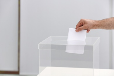 Man putting his vote into ballot box at polling station, closeup. Space for text