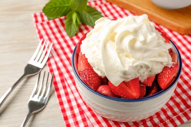 Photo of Bowl with delicious strawberries and whipped cream served on wooden table, closeup