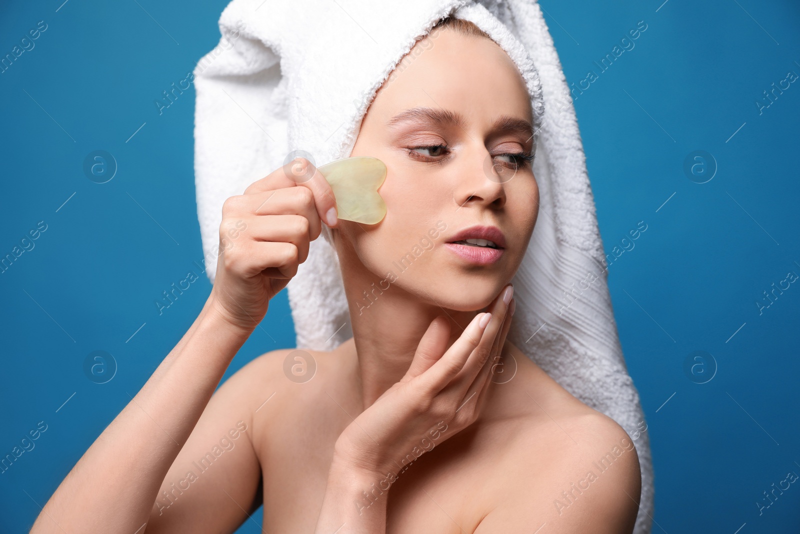 Photo of Beautiful young woman doing facial massage with gua sha tool on blue background