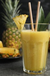 Photo of Tasty pineapple smoothie and fruit on grey table, closeup