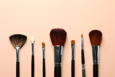 Different makeup brushes on light beige background, flat lay . Space for text