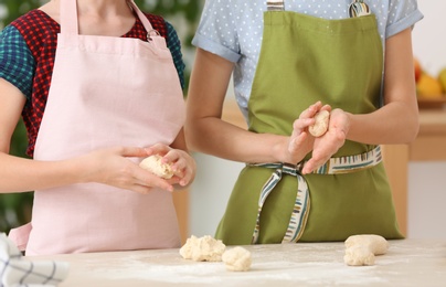 Mother and her daughter preparing dough at table, closeup