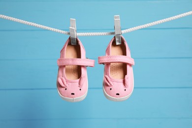 Photo of Cute baby shoes drying on washing line against light blue wooden wall