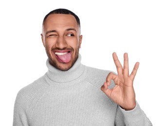 Photo of Happy young man showing his tongue and OK gesture on white background