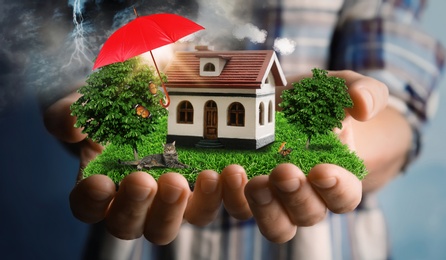 Image of Insurance concept - umbrella demonstrating protection. Woman holding house model with green lawn, closeup