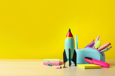 Bright toy rocket and school supplies on wooden table. Space for text