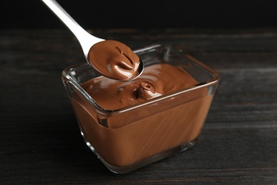 Spoon with tasty chocolate cream over glass bowl on wooden table