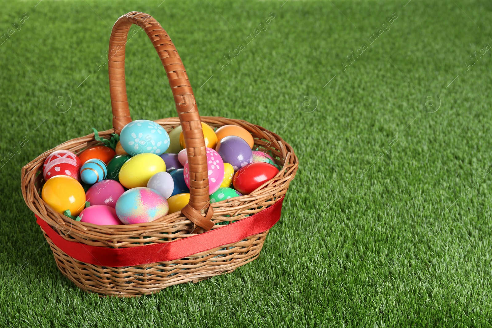 Photo of Wicker basket with Easter eggs on green grass. Space for text