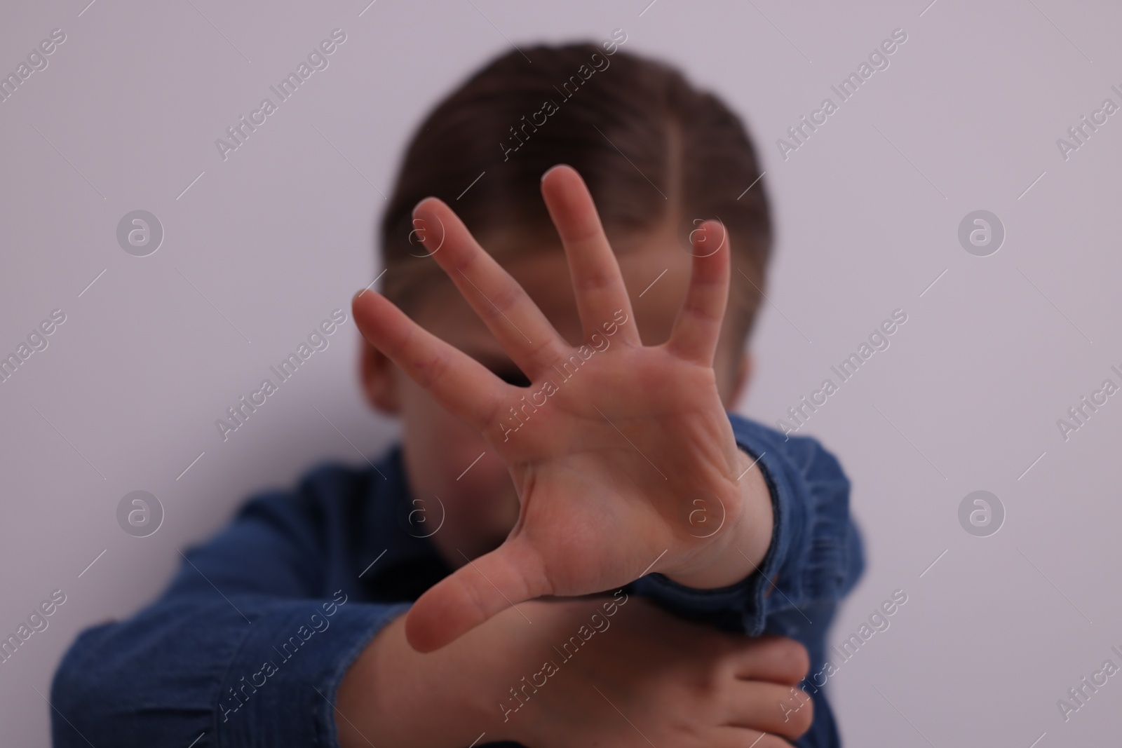 Photo of Child abuse. Girl making stop gesture near grey wall, selective focus