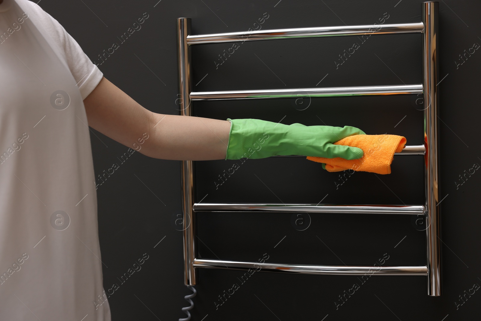 Photo of Woman cleaning heated towel rail with rag, closeup