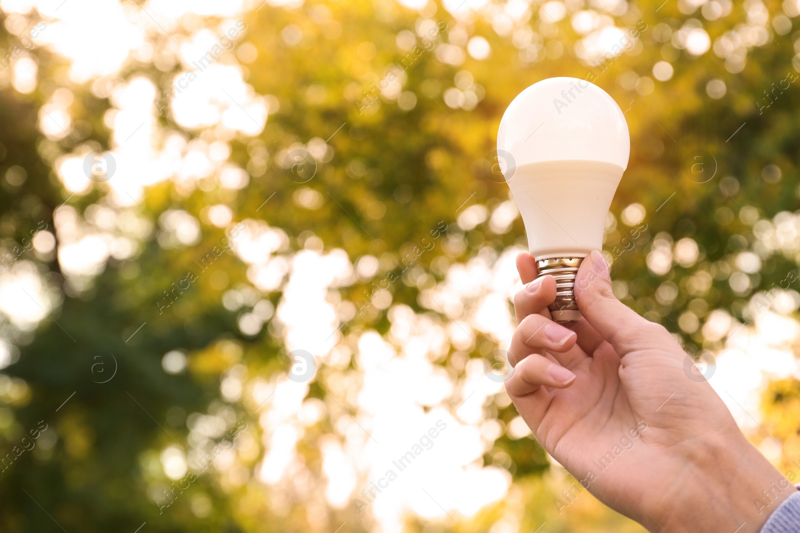 Photo of Woman holding lamp bulb outdoors, closeup. Space for text