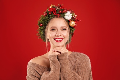 Photo of Beautiful young woman wearing Christmas wreath on red background