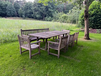 Photo of Wooden table with bench and chairs in garden. Landscape design