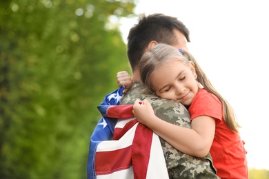 Father in military uniform with American flag hugging his little daughter at green park