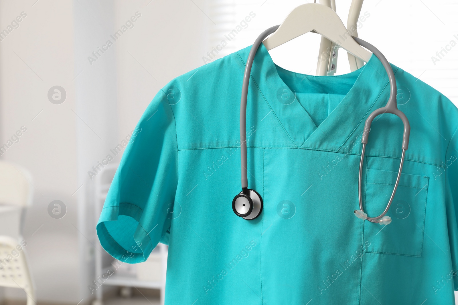Photo of Turquoise medical uniform and stethoscope on rack in clinic, closeup