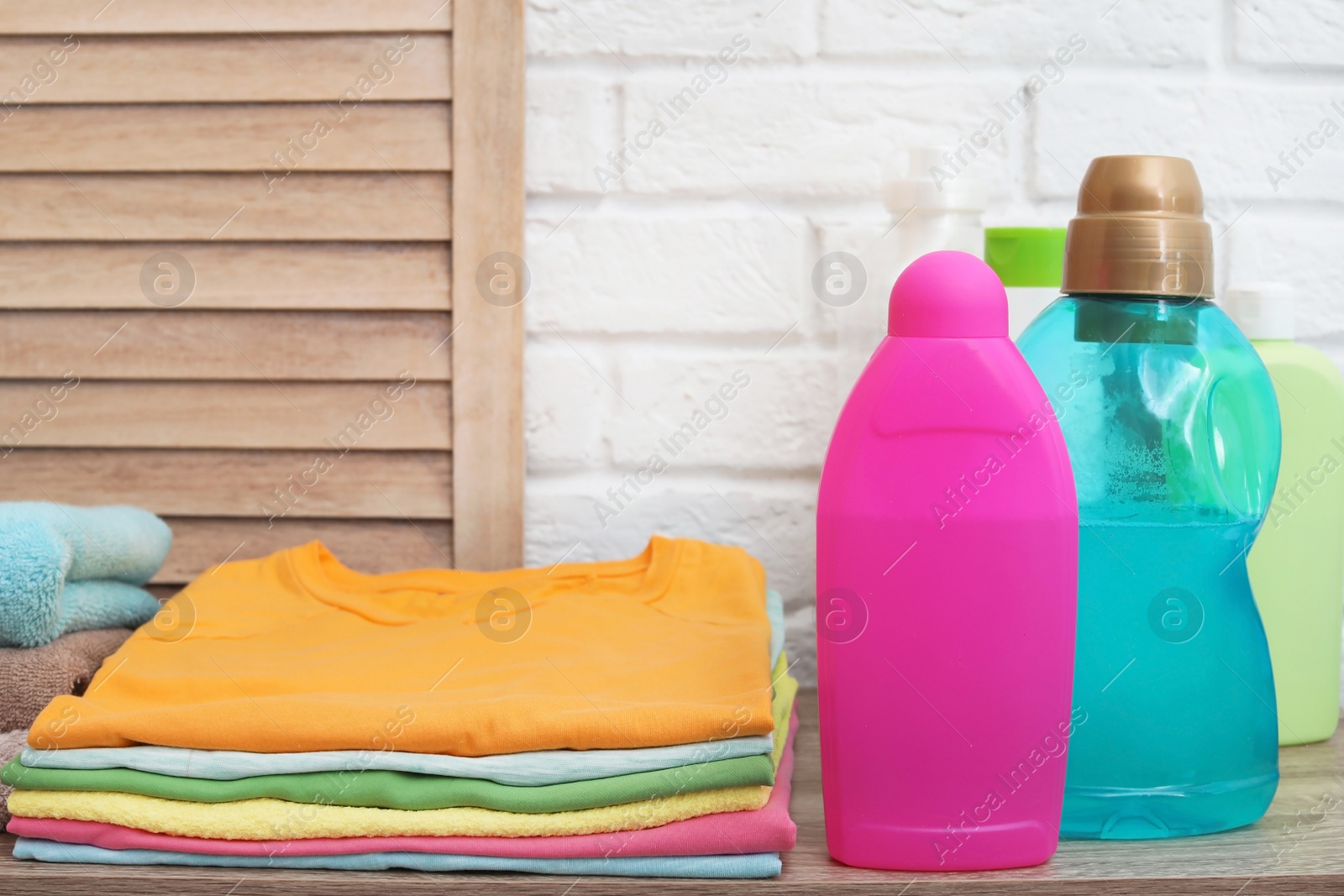 Photo of Clean clothes, towels and bottles with detergents on table