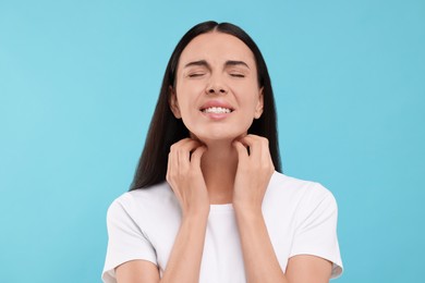 Photo of Suffering from allergy. Young woman scratching her neck on light blue background
