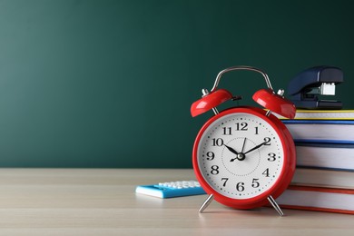 Photo of Alarm clock and different stationery on wooden table near green chalkboard, space for text. School time
