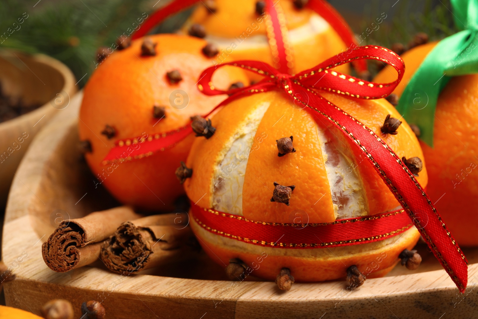 Photo of Pomander balls with ribbons made of fresh tangerines and cloves in wooden plate, closeup