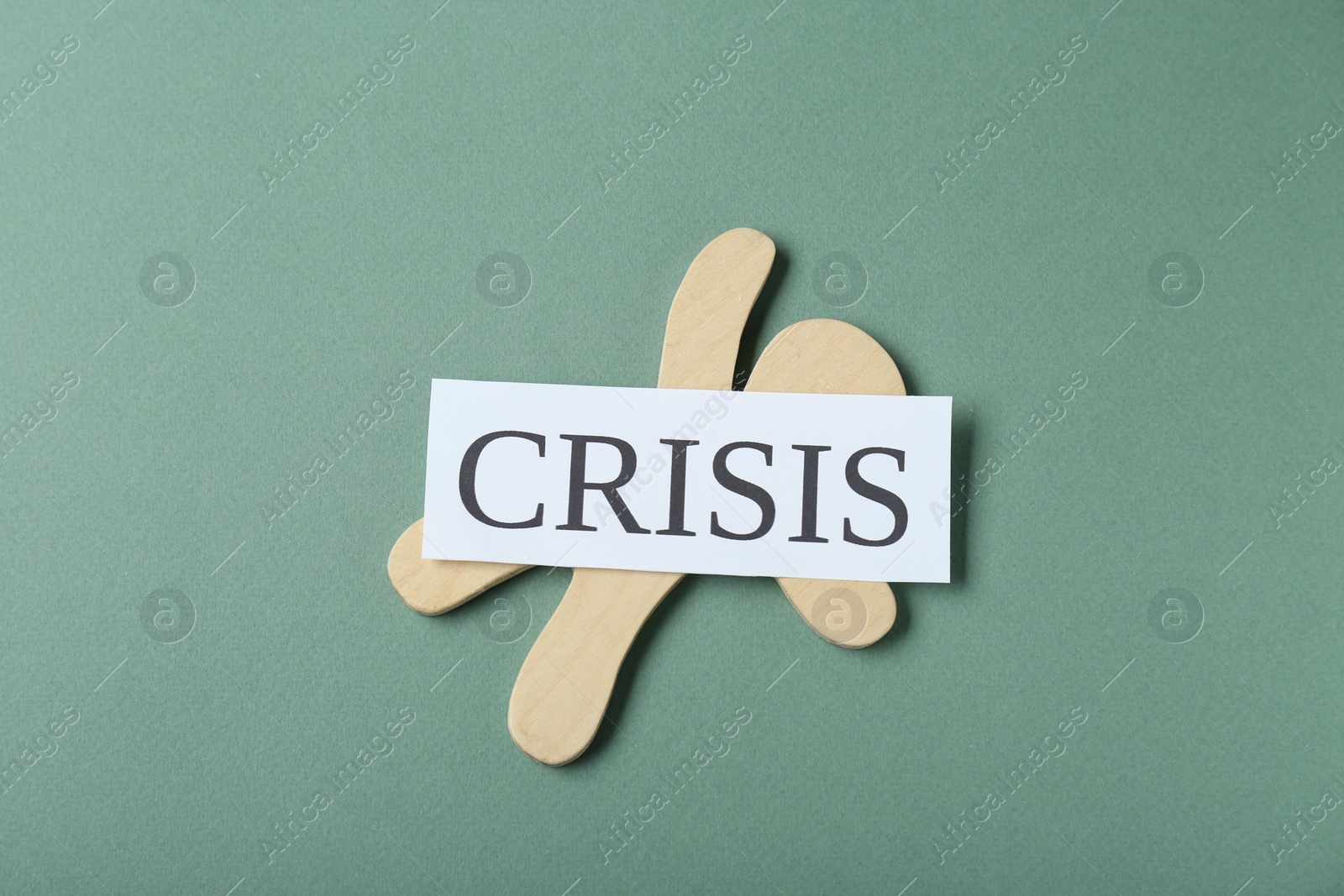 Photo of Wooden human figure and word Crisis on green background, top view
