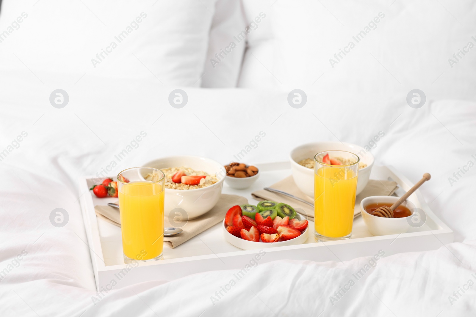 Tasty breakfast served in bed. Oatmeal, juice, fruits and honey on tray Photo of Tasty breakfast served in bed. Oatmeal, juice, fruits and honey on tray
