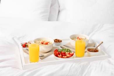 Photo of Tasty breakfast served in bed. Oatmeal, juice, fruits and honey on tray