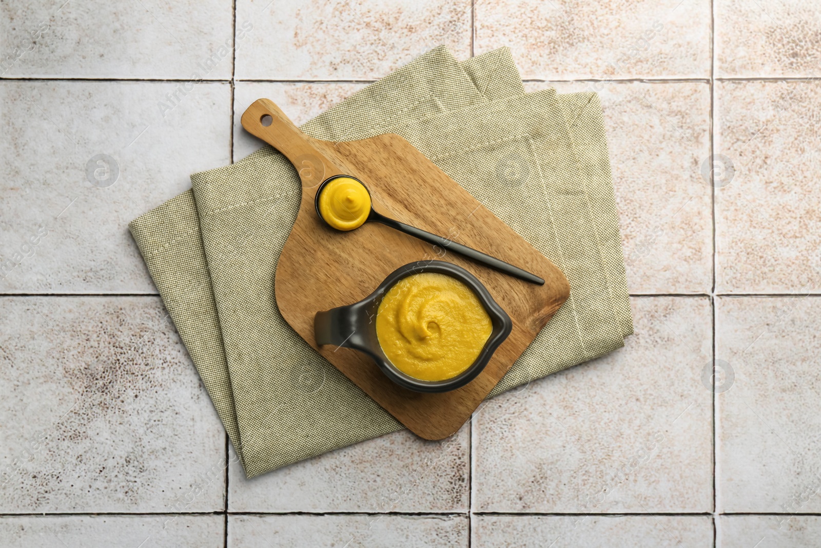 Photo of Tasty mustard sauce on light tiled table, top view