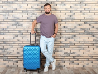 Photo of Man with suitcase near brick wall. Vacation travel
