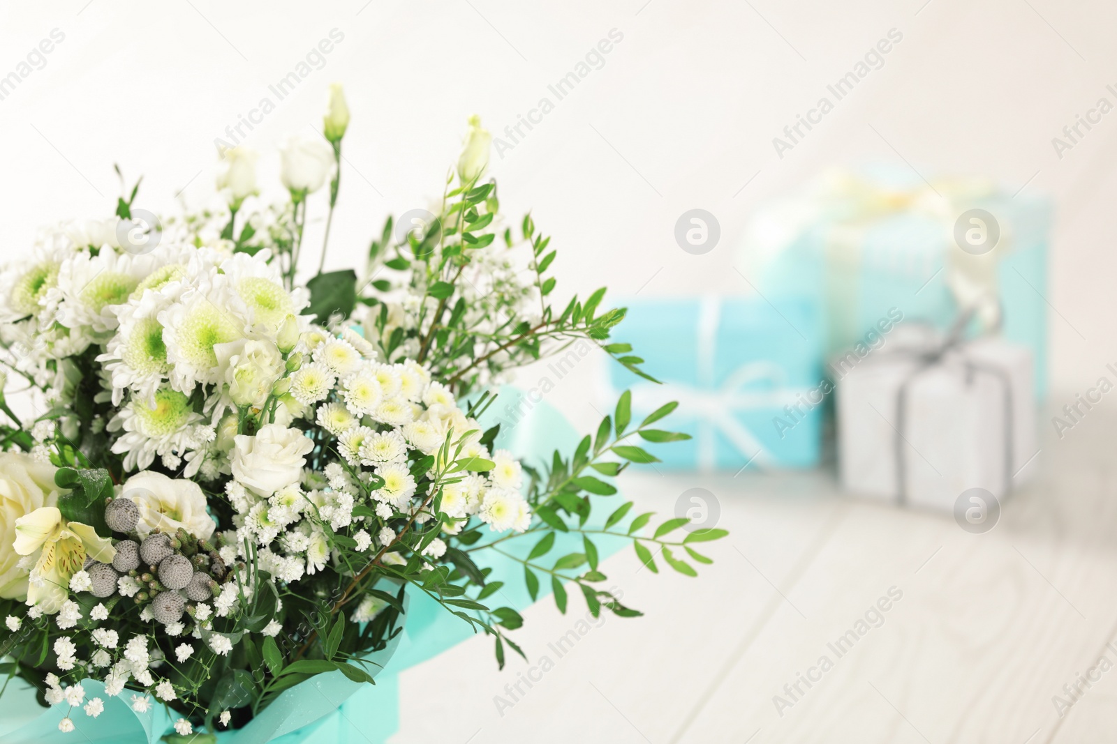 Photo of Beautiful bouquet of flowers and blurred gifts on background. Space for text