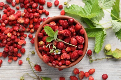 Photo of Fresh wild strawberries, flower and leaves on white wooden table, flat lay