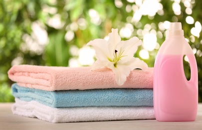 Photo of Pile of fresh towels, flower and detergent on table against blurred background