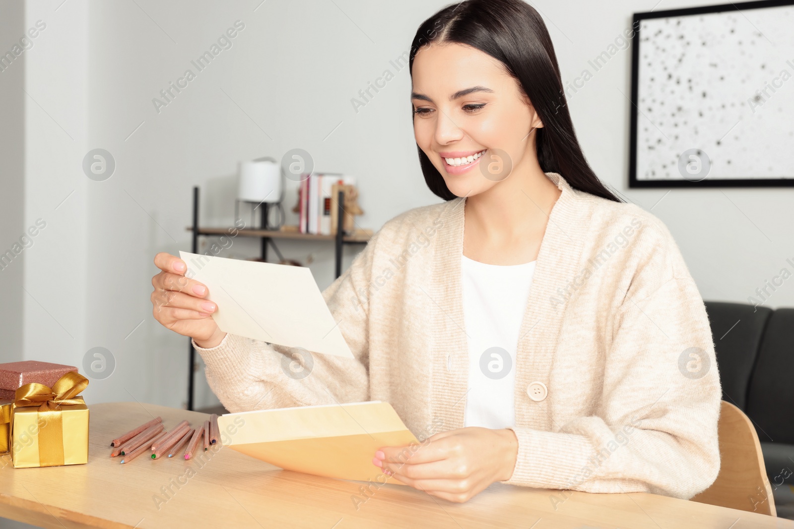 Photo of Happy woman reading greeting card at wooden table in room