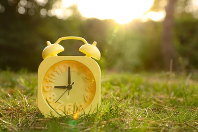 Photo of Yellow alarm clock on green grass outdoors. Space for text