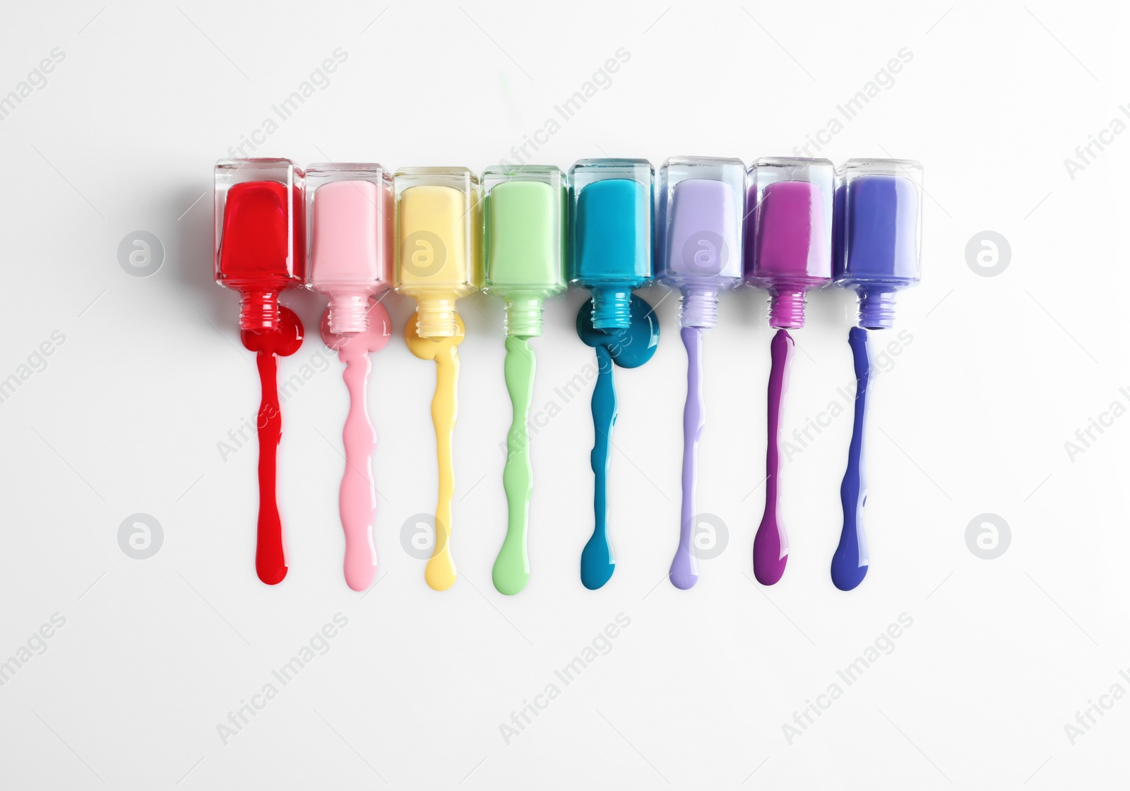 Photo of Spilled colorful nail polishes and bottles on white background, top view