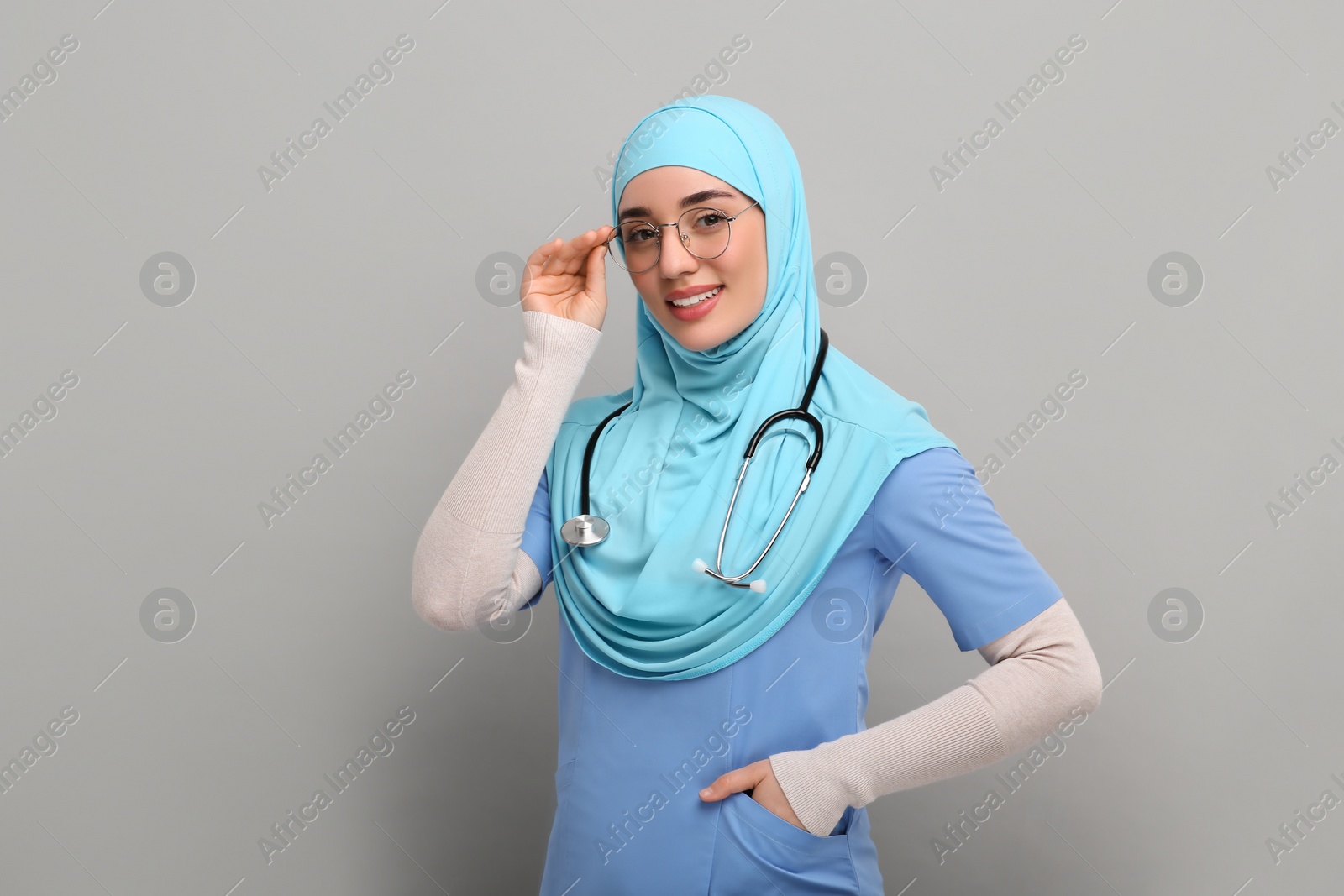 Photo of Muslim woman wearing hijab, medical uniform with stethoscope on light gray background