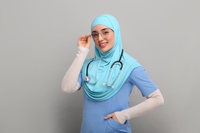 Photo of Muslim woman wearing hijab, medical uniform with stethoscope on light gray background