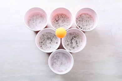 Photo of Plastic cups and ball for beer pong on white table, flat lay