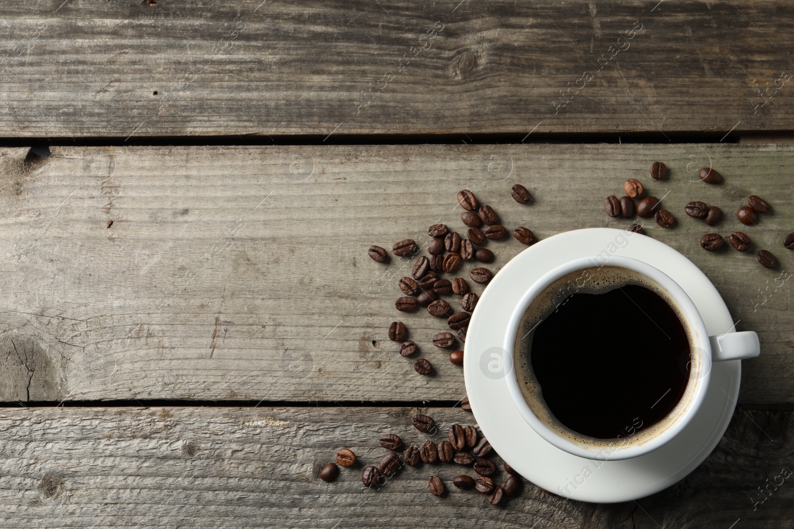 Photo of Cup of hot aromatic coffee and roasted beans on wooden table, flat lay. Space for text