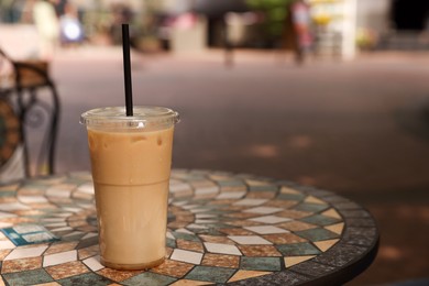 Photo of Takeaway plastic cup with cold coffee drink and straw on table outdoors, space for text